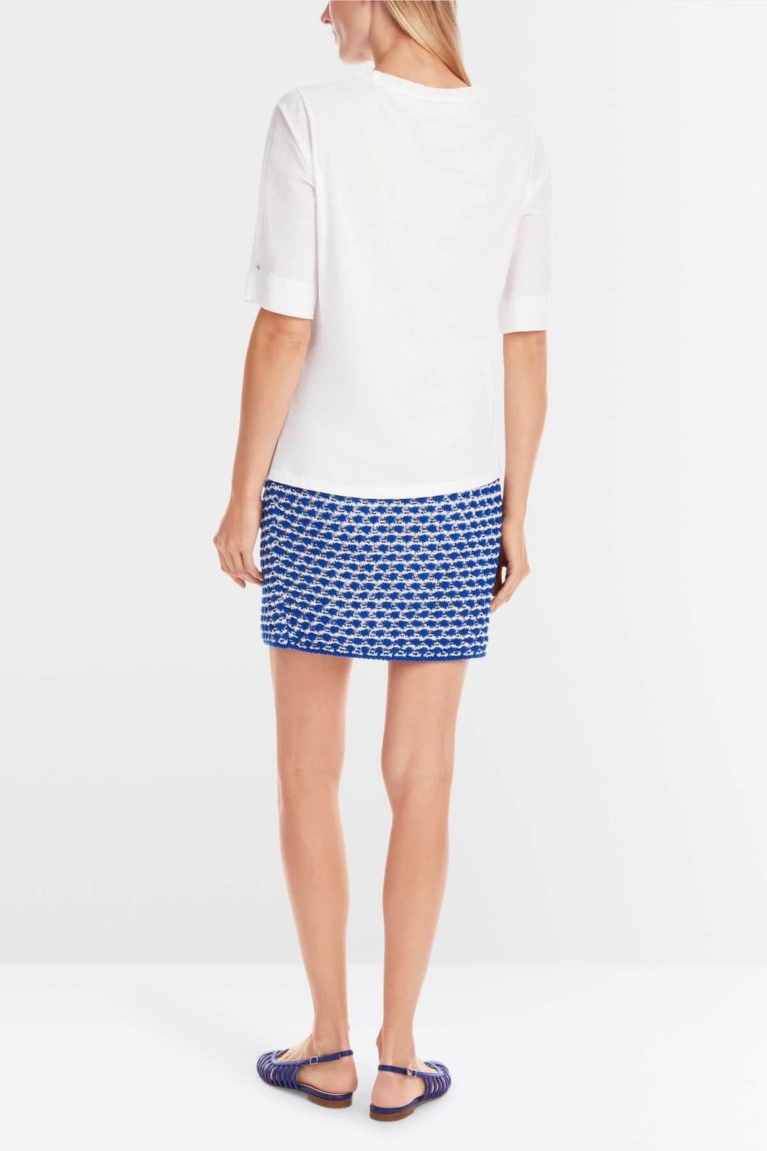 Femme vue de dos portant un t-shirt blanc avec une jupe bleue à motifs, style estival élégant.