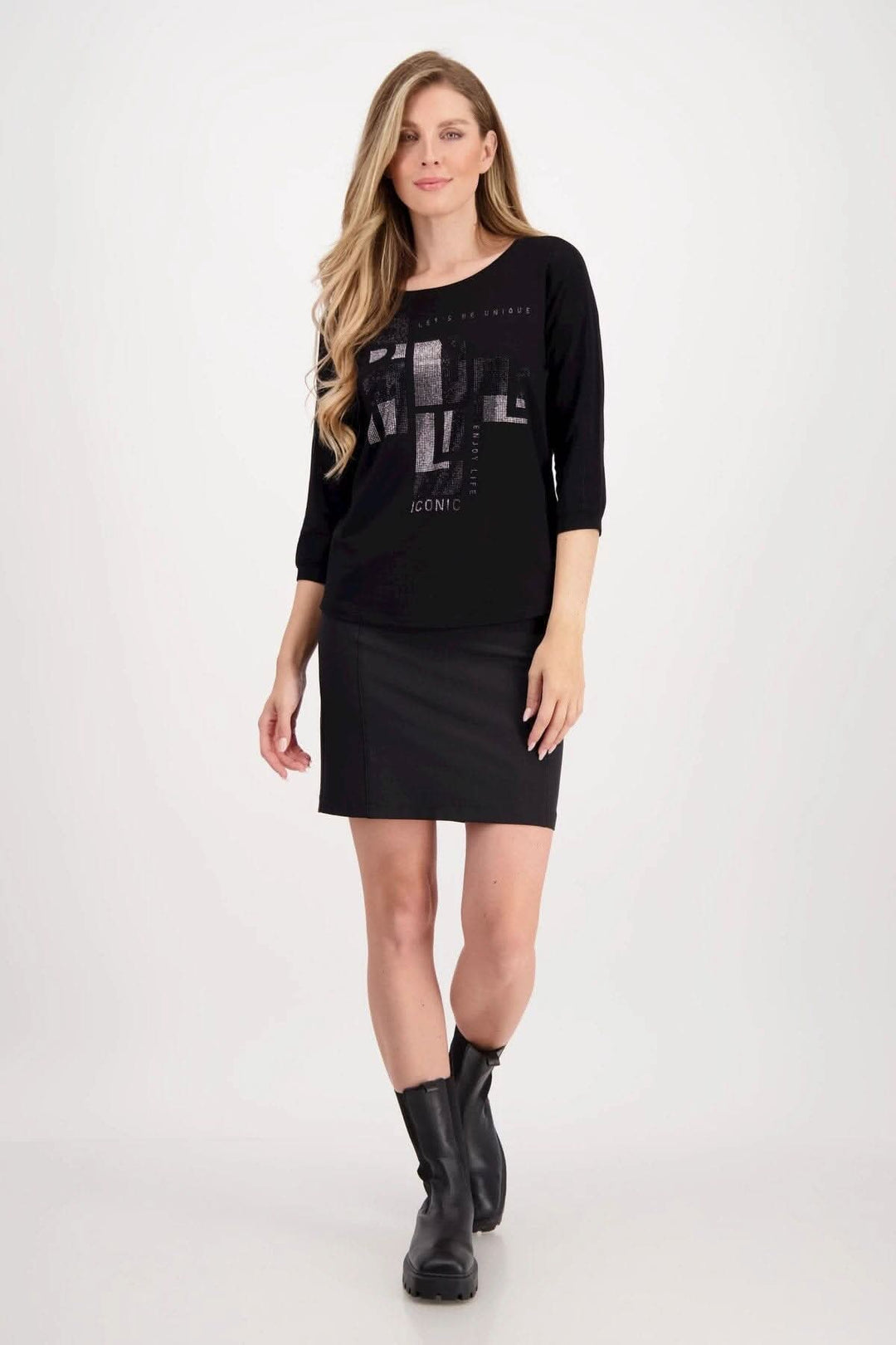 Haut Monari noir à lettrage décoratif, manches 3/4, porté avec une jupe noire et des bottes, style décontracté.