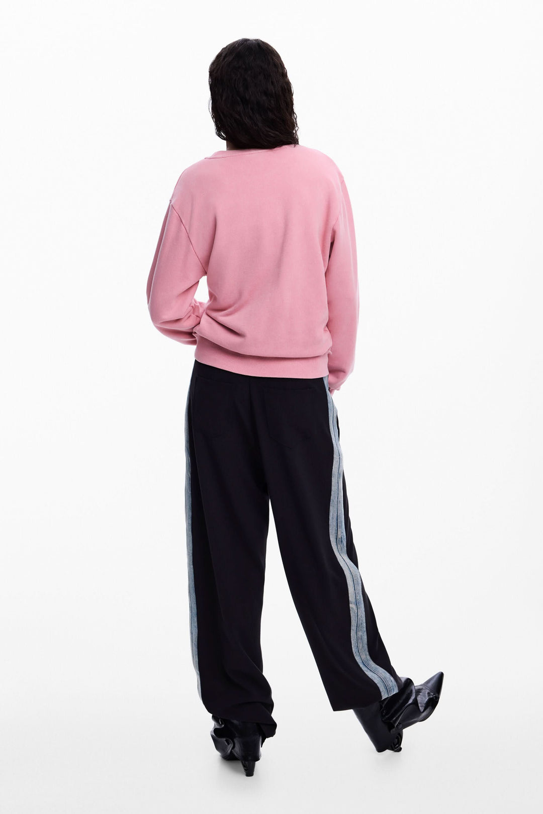 Femme portant un chandail rose avec logo et perles, vue arrière, coupe décontractée, manches longues, look moderne et créatif.