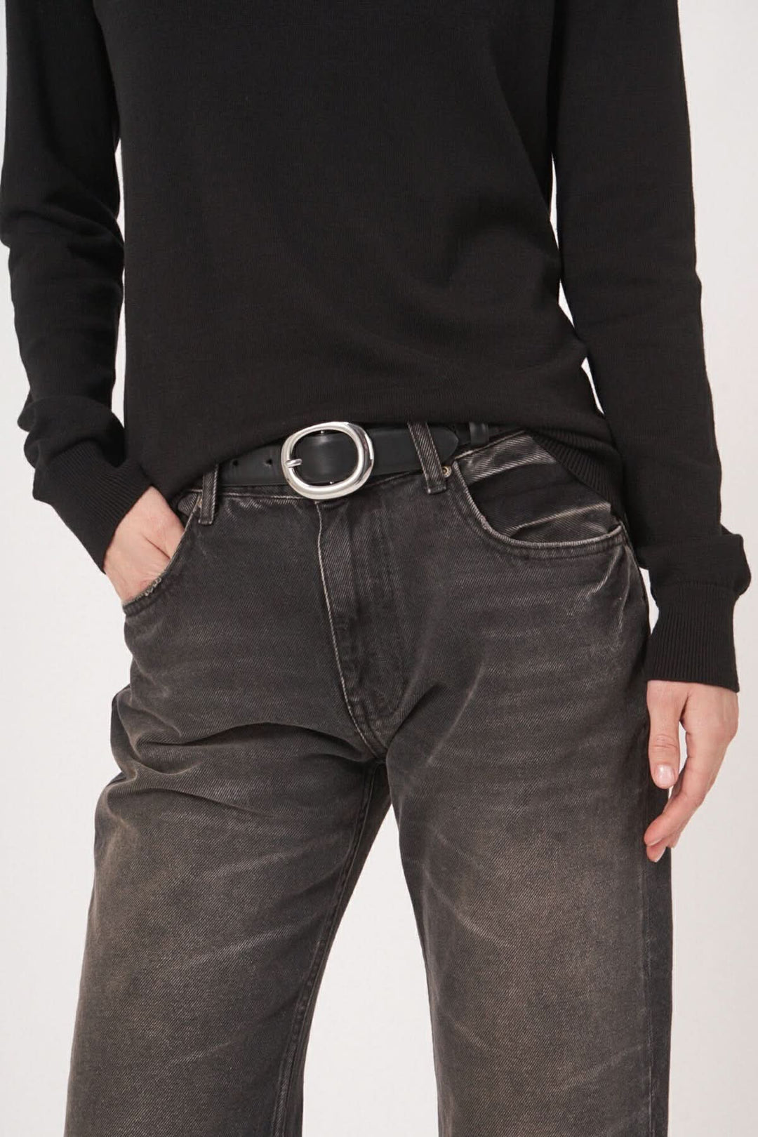 Chandail basique noir à encolure bateau avec ceinture en métal et jean délavé pour un look minimaliste.