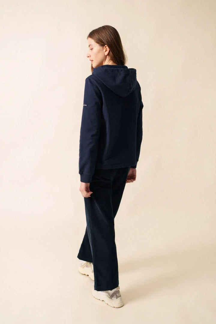 Femme portant un chandail à capuche marin avec rayures sur une fond neutre, style décontracté chic.