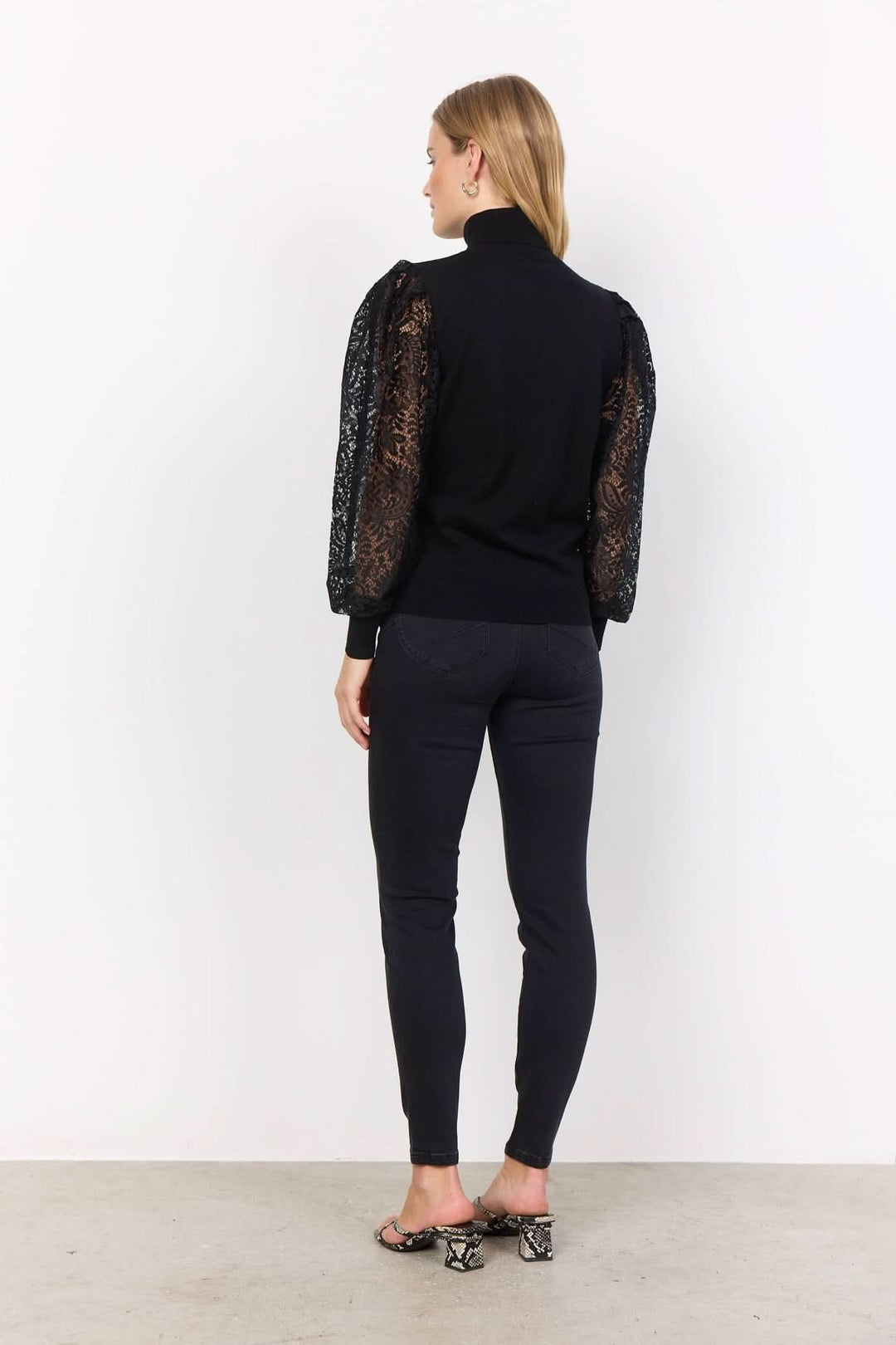Chandail à col montant en noir avec manches en dentelle transparent, style chic et féminin.