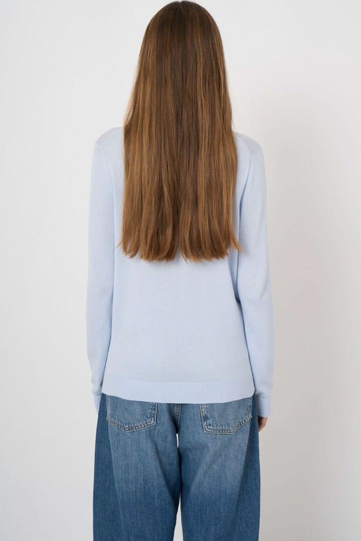 Femme portant un chandail col en V manches longues, dos à la caméra, avec un jean décontracté, style polyvalent et intemporel.
