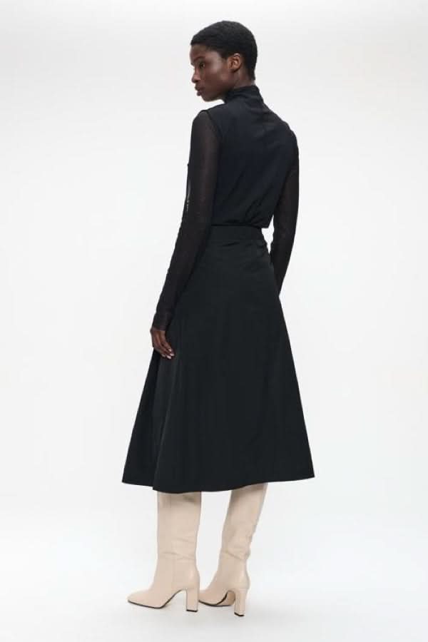 Femme portant un chandail à col montant et manches transparentes, style chic et moderne, arrière-plan blanc.