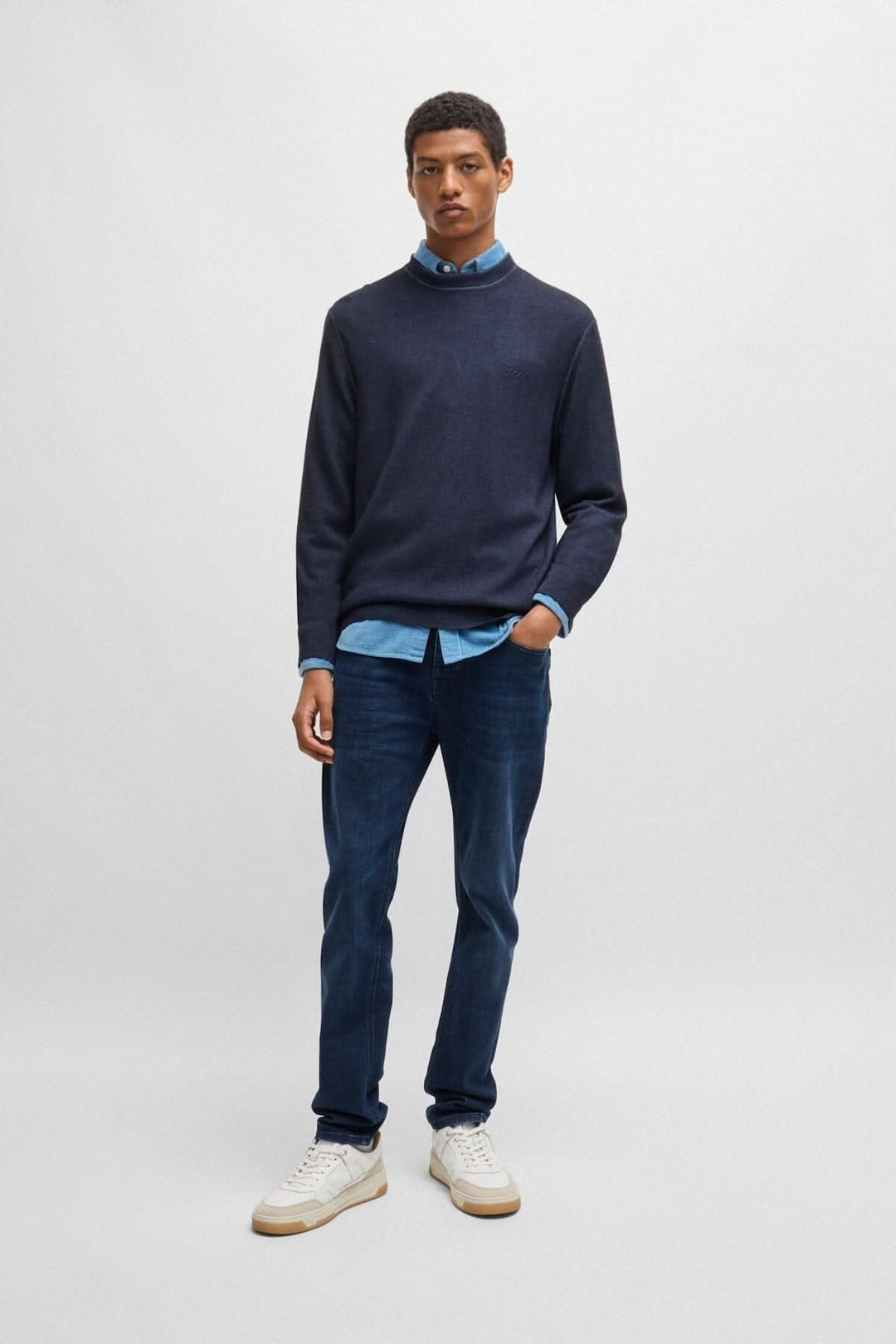 Homme portant un chandail col rond en laine navy avec une chemise bleu en dessous et un jean, style décontracté.