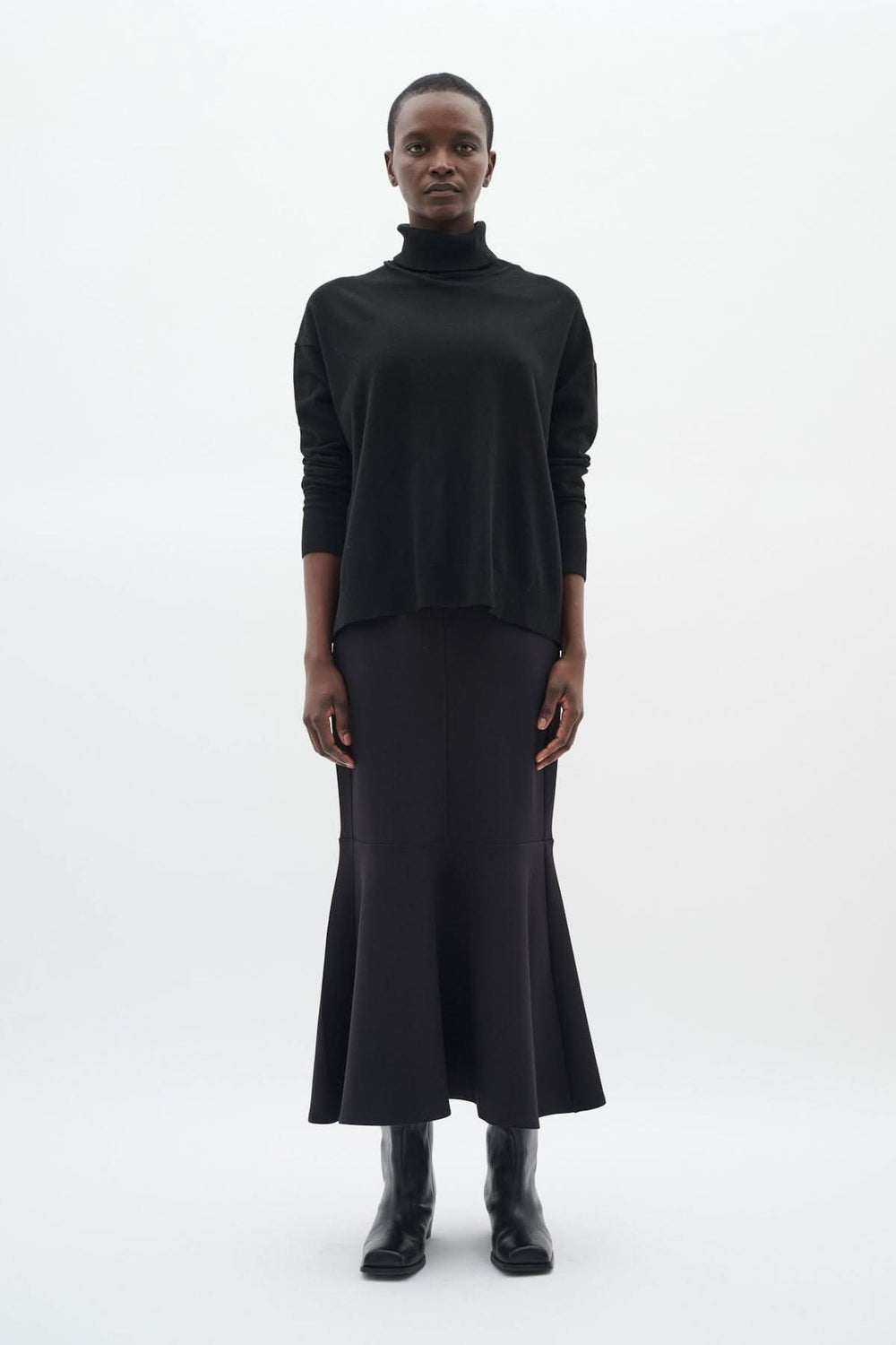 Femme portant un chandail à col roulé décontracté noir avec une jupe longue noire et des bottes, look chic.