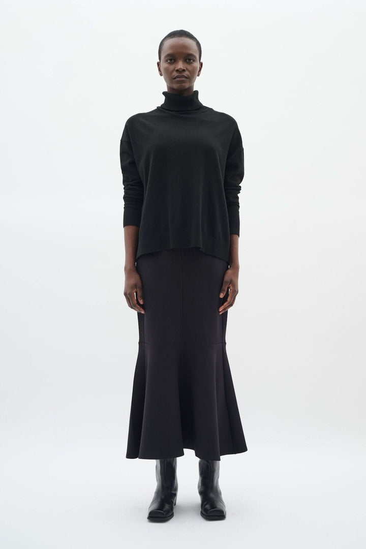 Femme portant un chandail à col roulé décontracté noir avec une jupe longue noire et des bottes, look chic.