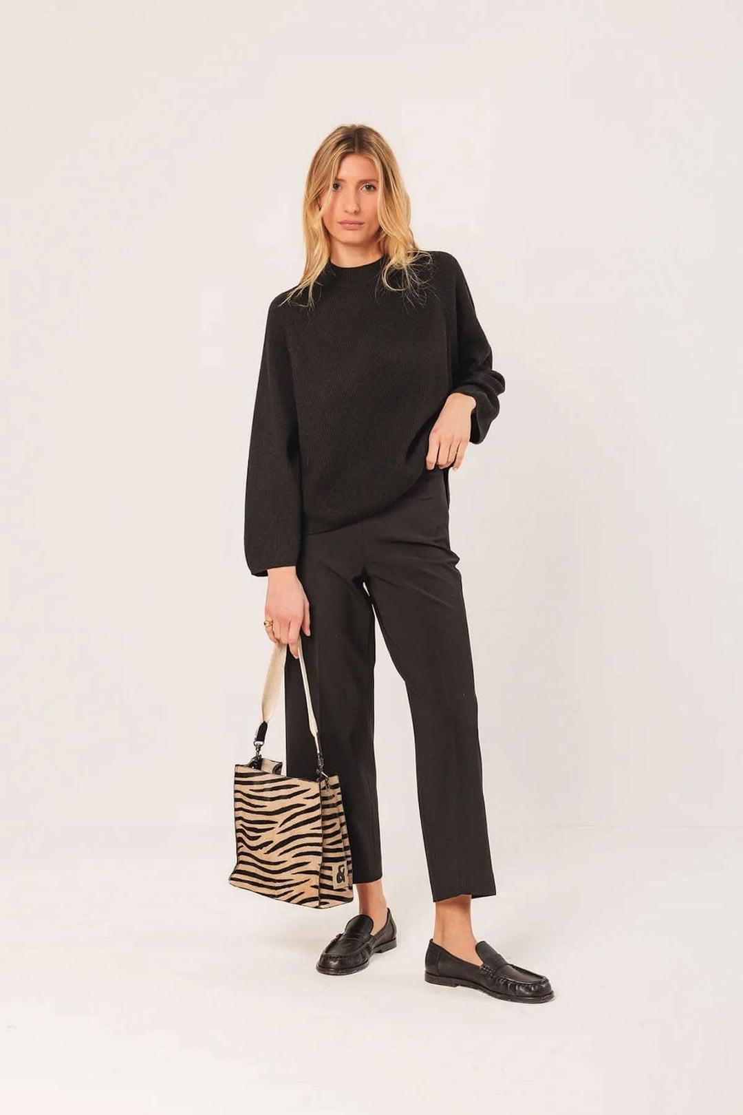 Femme portant un chandail côtelé noir avec un pantalon noir et un sac à main zébré, en style chic et décontracté.