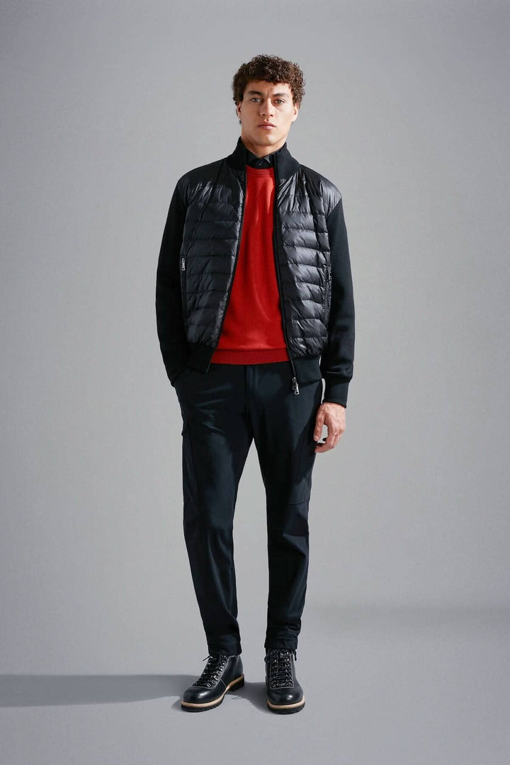 Homme portant un chandail rouge et une veste noire avec un pantalon noir, affichant un look moderne et élégant.