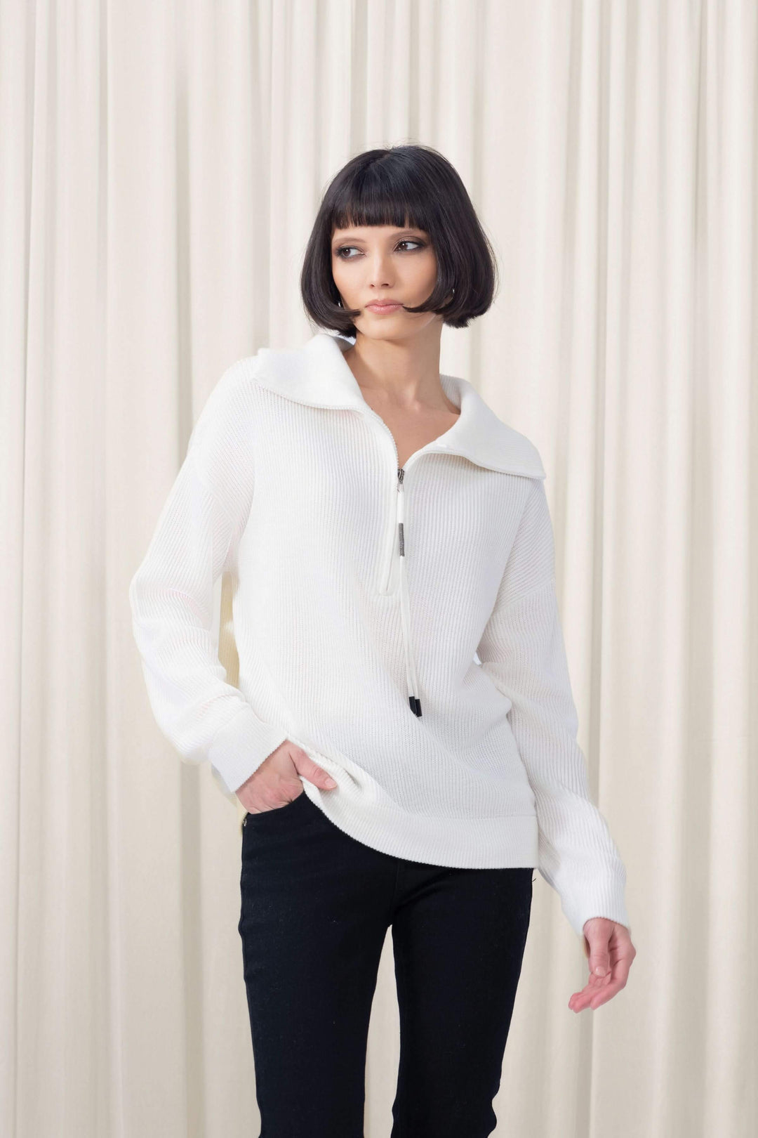 Femme portant un chandail demi-glissière blanc avec col large et maille texturée pour un style moderne et élégant.