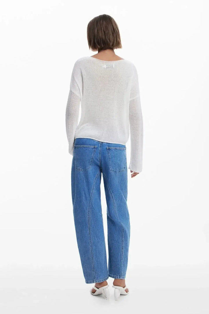 Femme vue de dos portant un chandail en maille fine blanc et un jean bleu, style décontracté et moderne.