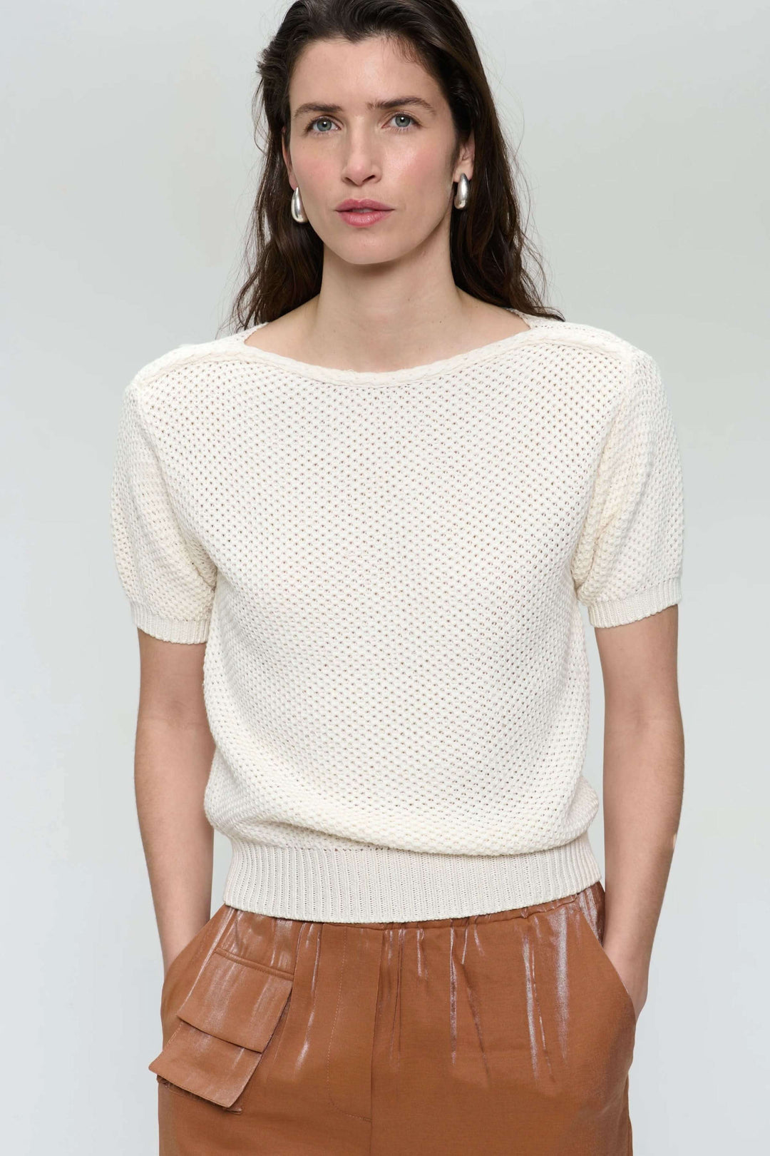 Chandail en tricot ajouré blanc avec encolure bateau et manches courtes, porté avec un pantalon marron.