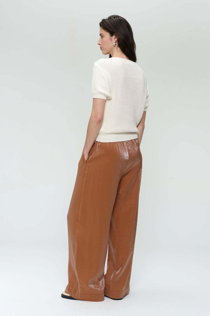 Femme vue de dos portant un chandail en tricot ajouré avec un pantalon large marron, style décontracté et élégant.