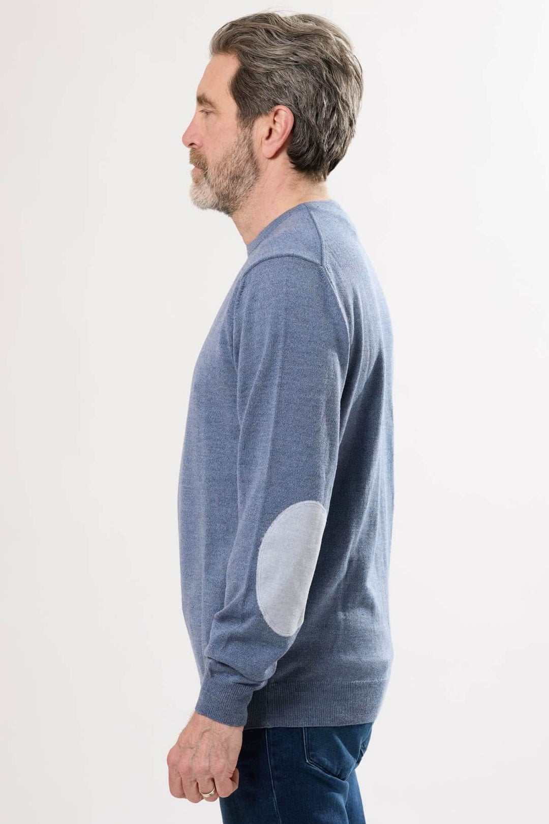 Homme portant un chandail en tricot bleu avec coudières contrastantes, profil latéral d'une allure intemporelle.