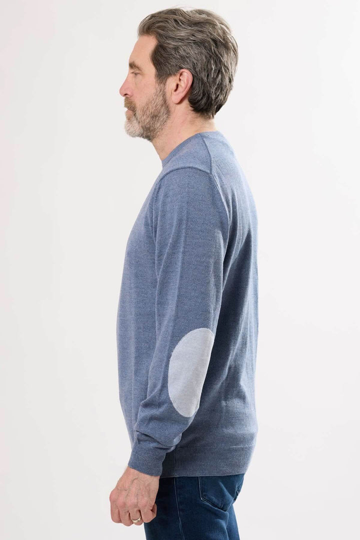 Homme portant un chandail en tricot bleu avec coudières contrastantes, profil latéral d'une allure intemporelle.