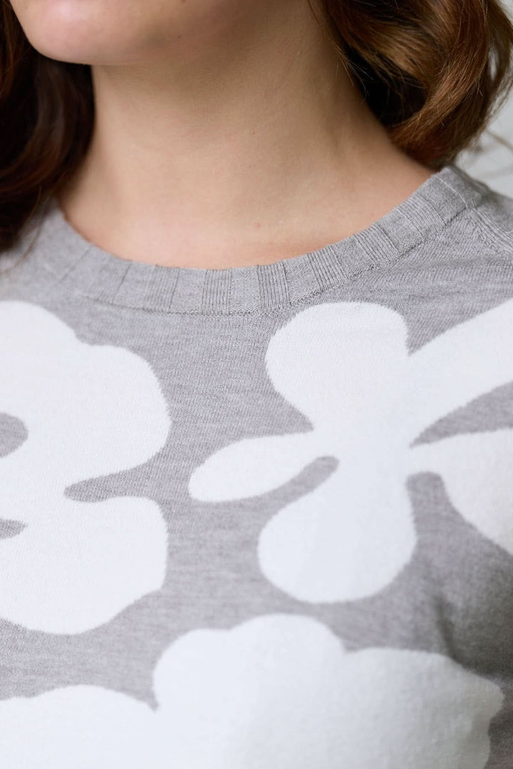 Chandail en tricot à motif floral avec encolure ronde et grandes fleurs blanches sur fond gris, détail en maille souple et confortable.