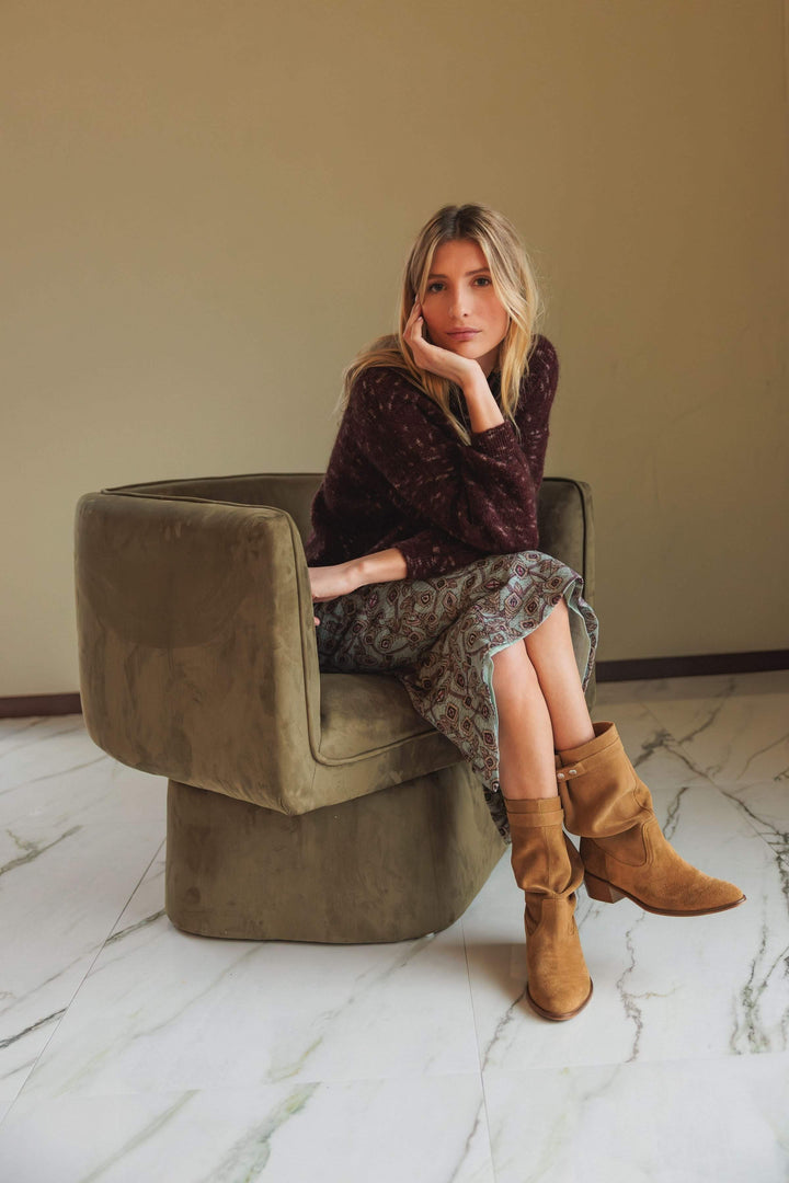 Femme assise dans un canapé olive, portant un chandail maille texturée et une jupe imprimée, style décontracté.