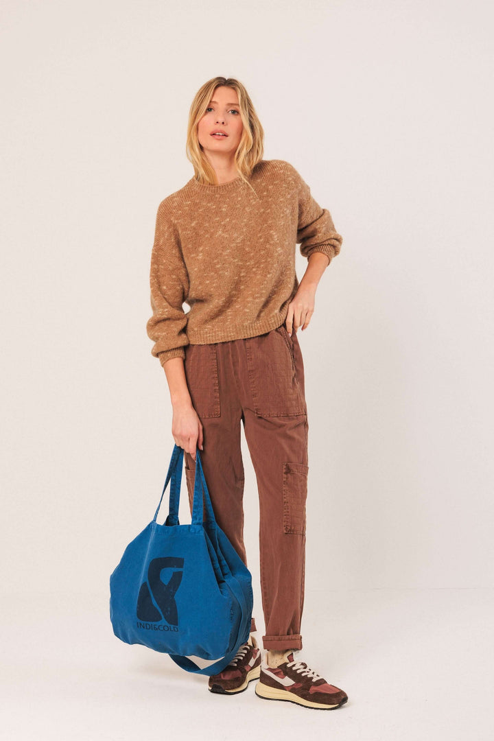 Modèle portant un chandail en maille texturée beige, pantalon marron, et sac bleu, style décontracté et tendance.