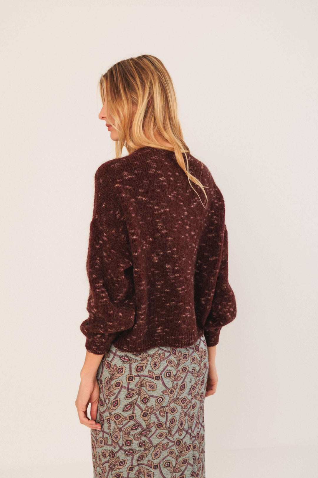 Femme portant un chandail maille texturée bordeaux avec manches bouffantes, associée à une jupe imprimée.