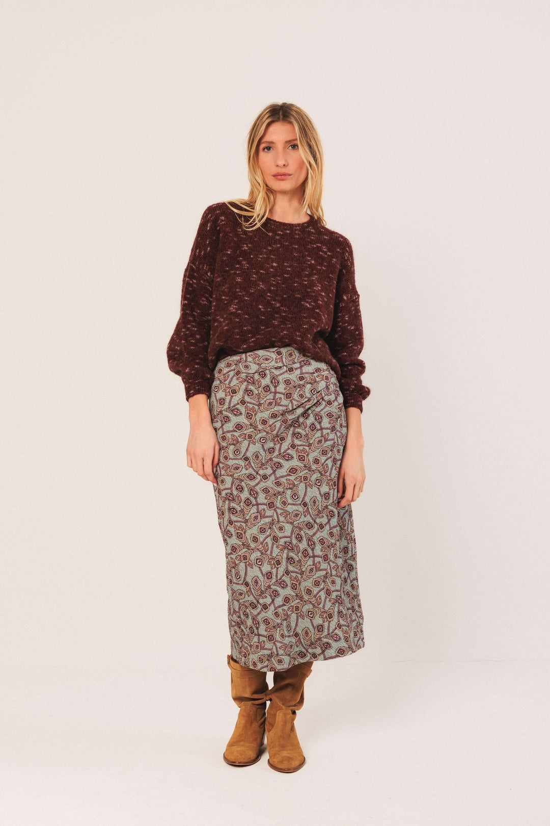 Femme portant un chandail maille texturée couleur bordeaux avec une jupe imprimée et des bottes marron.