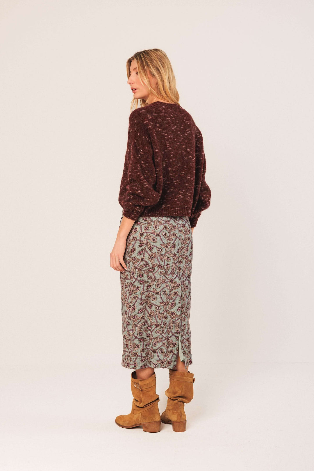 Femme portant un chandail maille texturée avec une jupe imprimée, style décontracté et tendance.