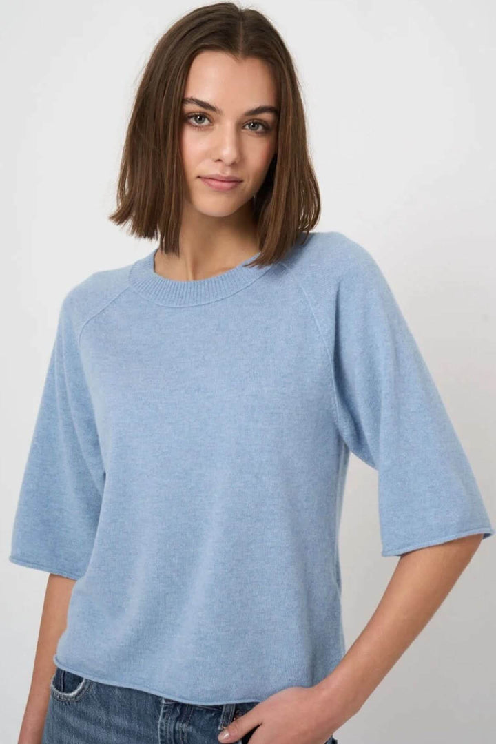 Femme portant un chandail à manches courtes bleu avec encolure ronde et coupe droite, idéal pour un style décontracté ou soigné.