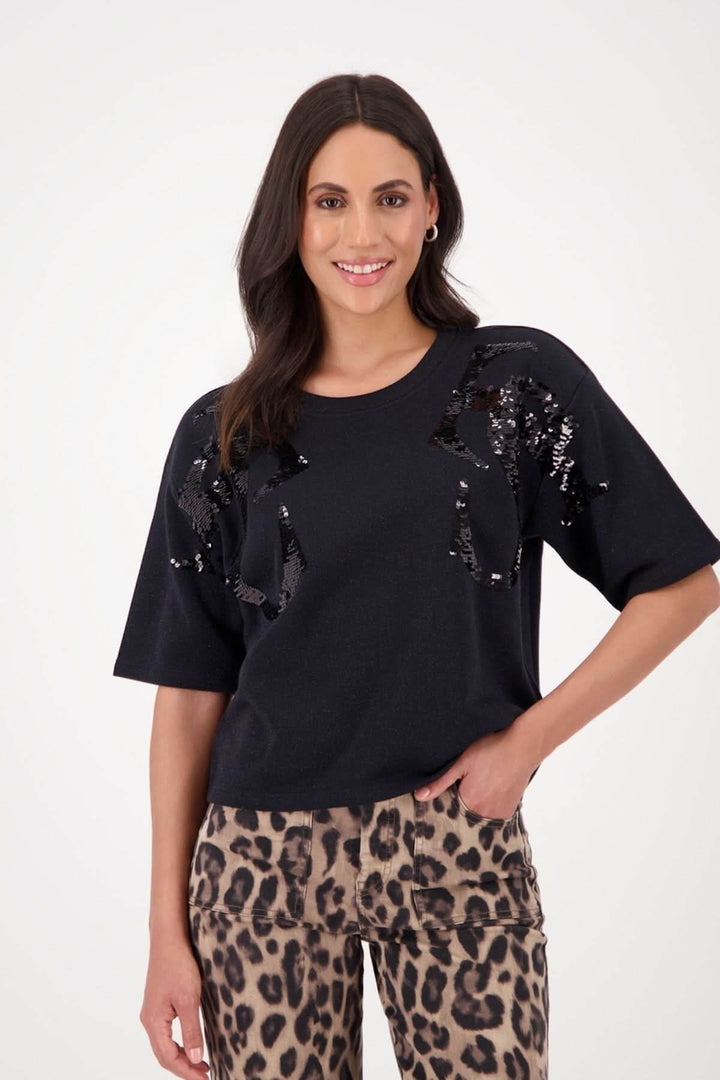 Femme portant un chandail à manches courtes noir avec paillettes et pantalon imprimé léopard.