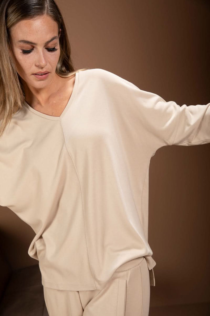 Femme portant un chandail minimaliste beige avec encolure en V et manches longues, design épuré pour un look moderne.