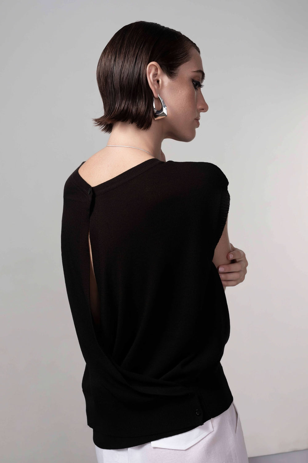 Femme portant un chandail ouverture au dos sans manches en maille fine, ajoutant une touche contemporaine et élégante à sa tenue.