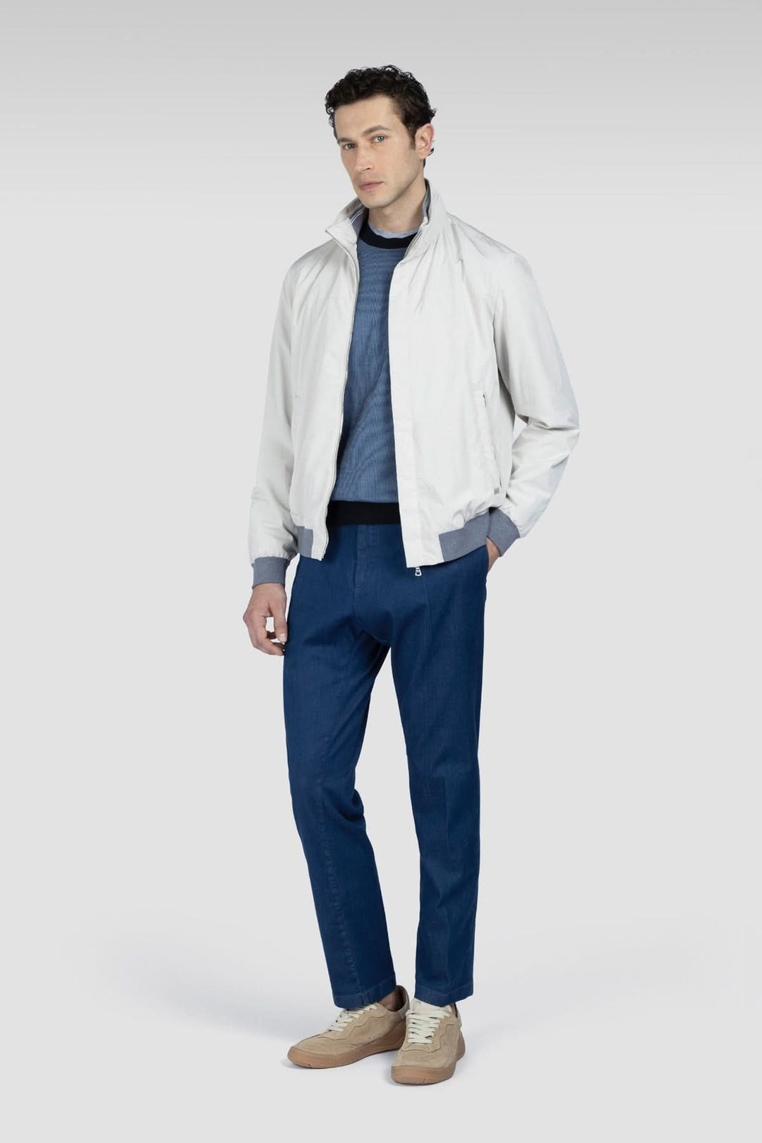 Homme en veste blanche avec un pull bleu et un pantalon bleu, stylé pour un look décontracté et moderne.
