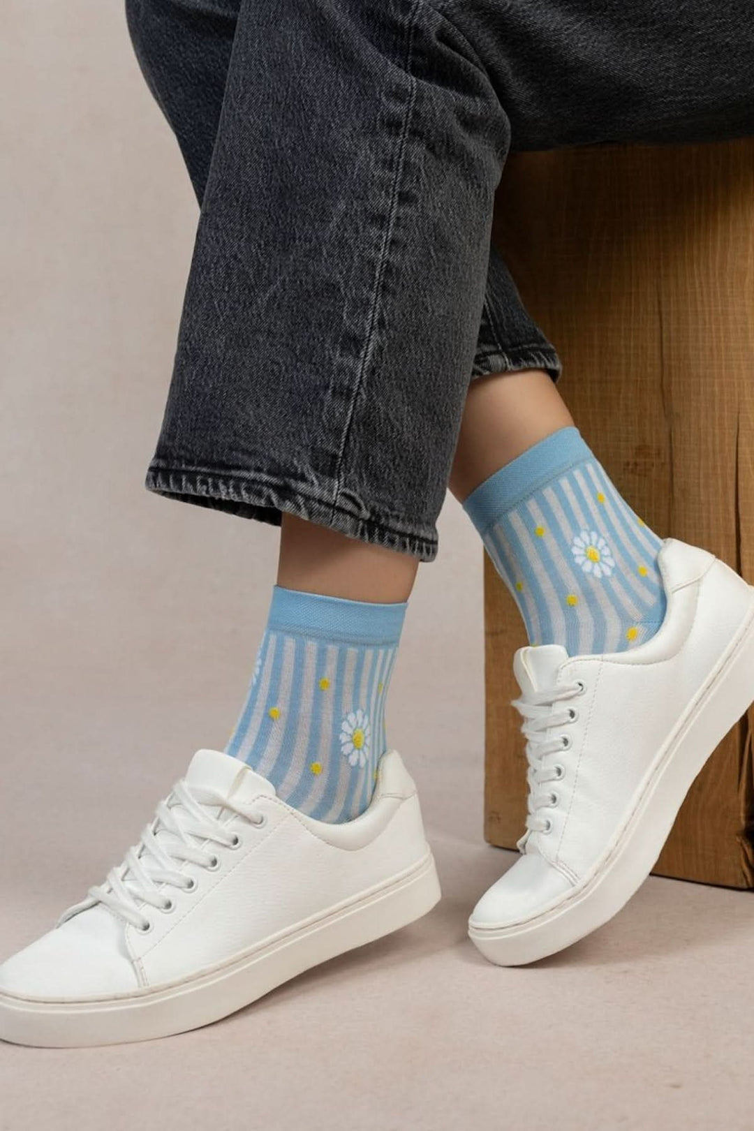 Chaussettes courtes à rayures bleues et marguerites, portées avec des chaussures blanches sur un fond neutre.