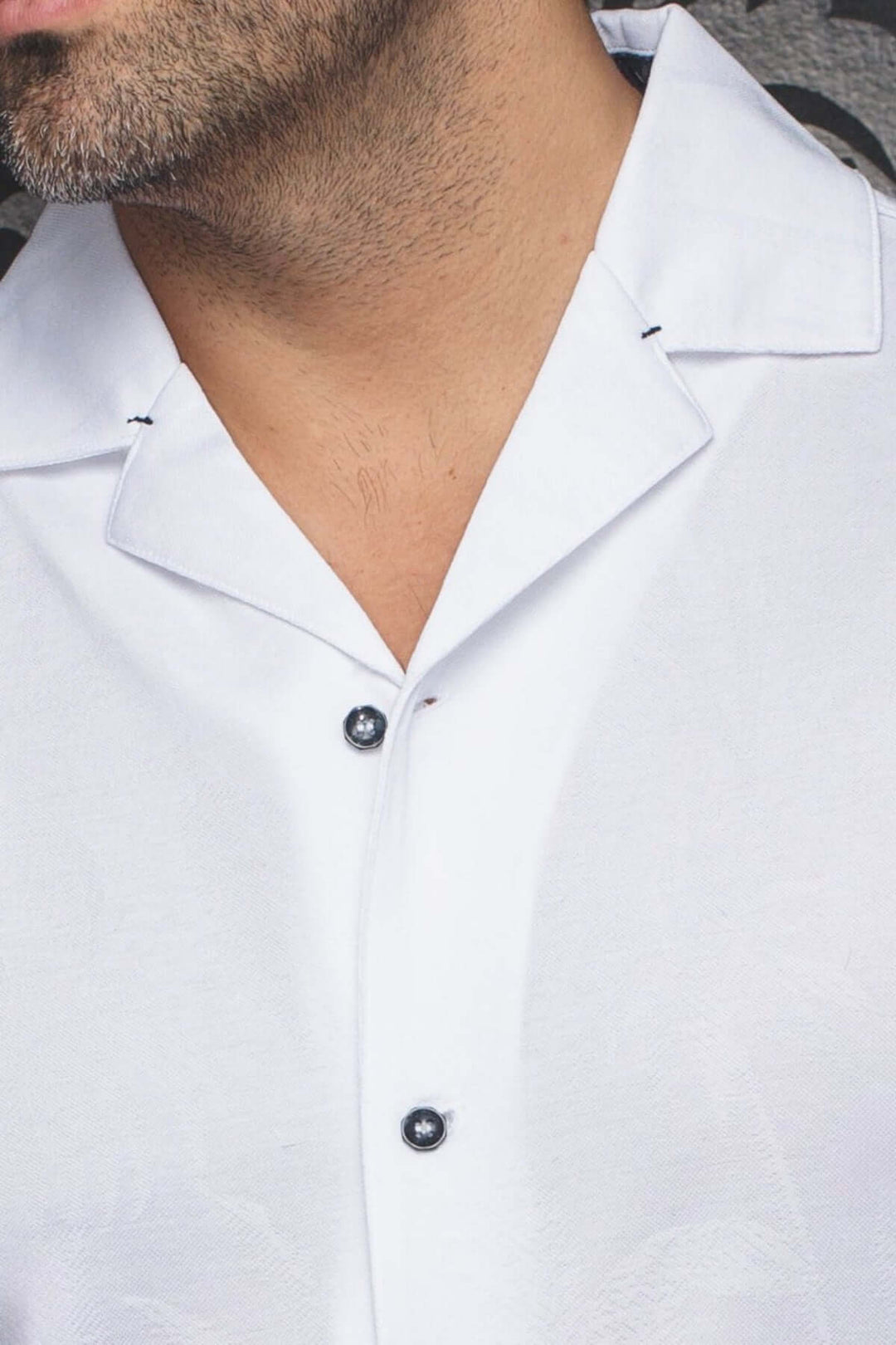Vue rapprochée d'une chemise blanche à col cubain et boutons, mettant en valeur sa texture subtile.
