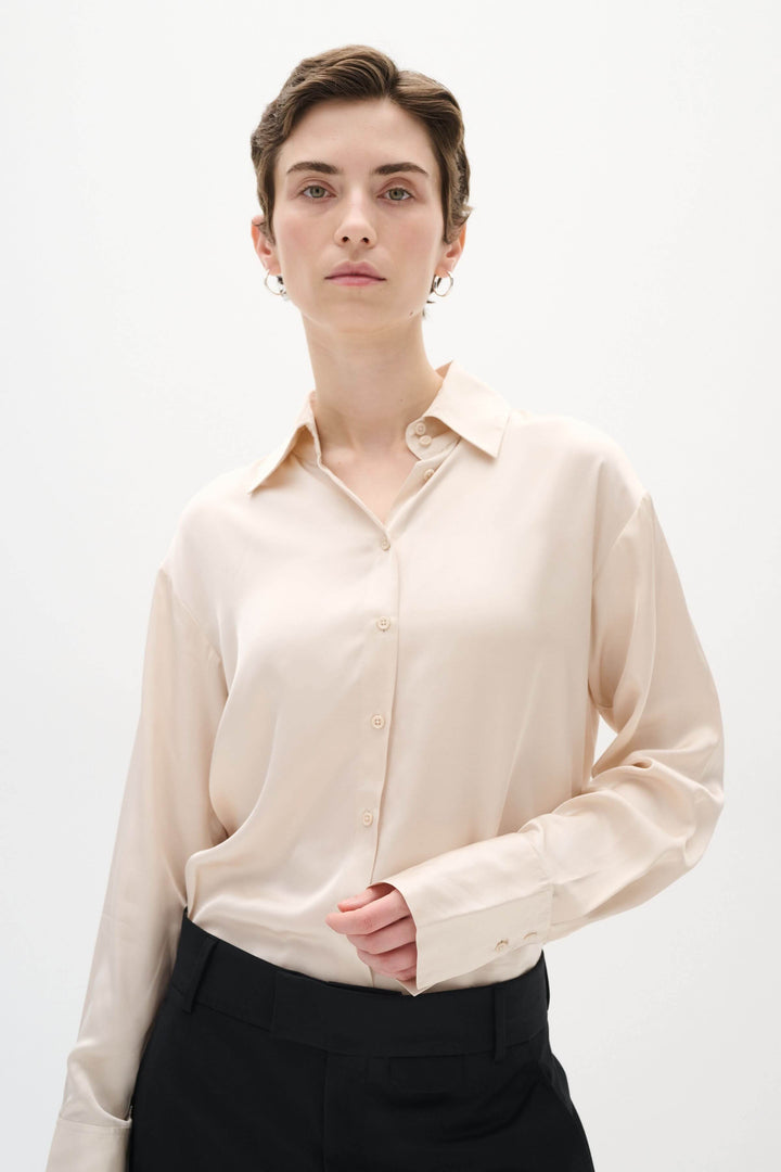 Chemise Pauline satinée, coupe ample, manches longues, style chic et décontracté, portée avec pantalon noir.