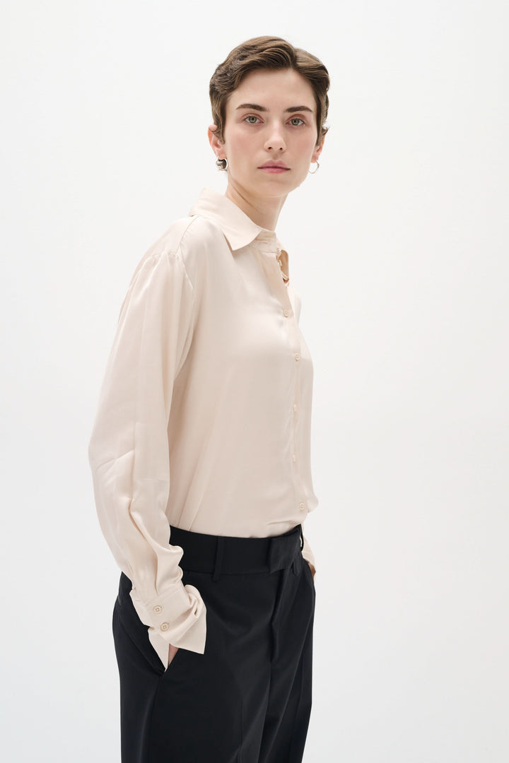 Chemise satinée Pauline, ample avec col de chemise, portée avec un pantalon noir, style chic.