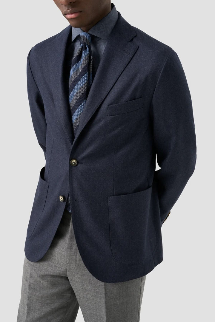 Homme portant un blazer bleu marine avec une chemise à rayures et un pantalon gris, pour un style formel élégant.