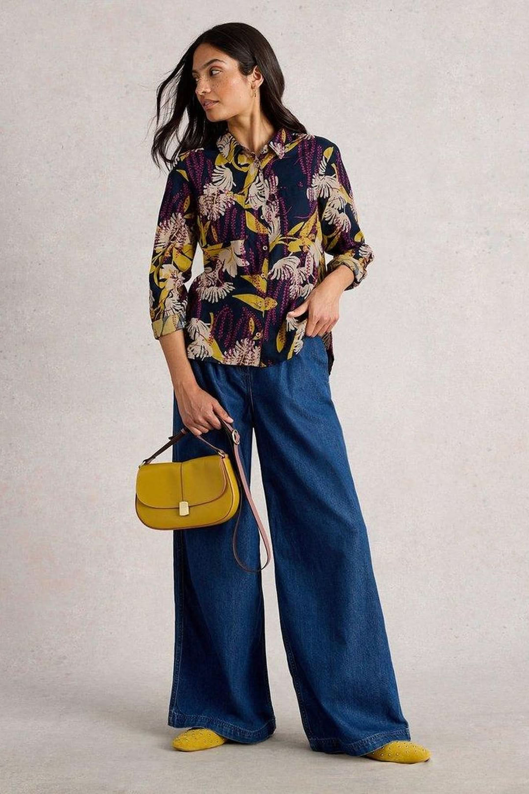 Femme portant chemise en coton manches retroussables avec motif floral, pantalon ample bleu et sac à main jaune pour un look décontracté.