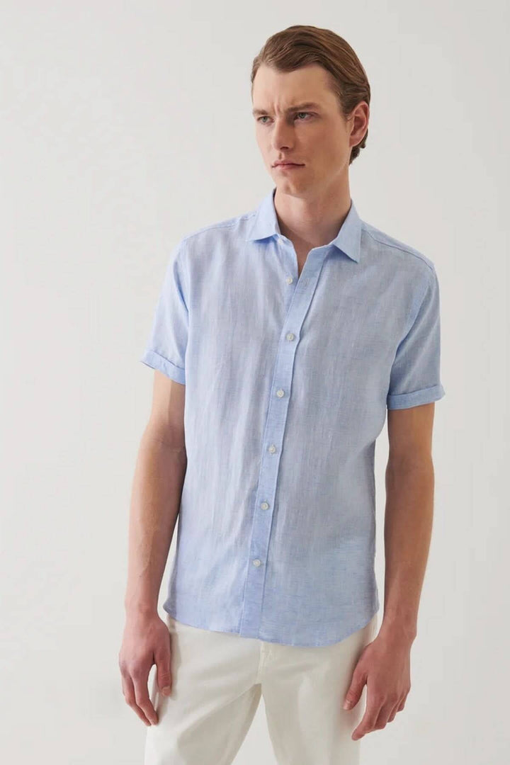 Chemise en lin à manches courtes, couleur chambray, col classique, boutons, style estival, portée avec pantalon clair.