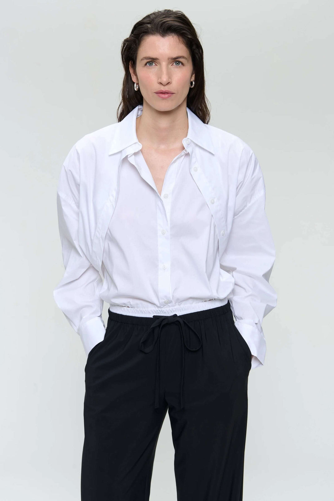 Chemise en popeline blanche avec coupe ample, col pointu et manches longues, portée avec un pantalon noir.