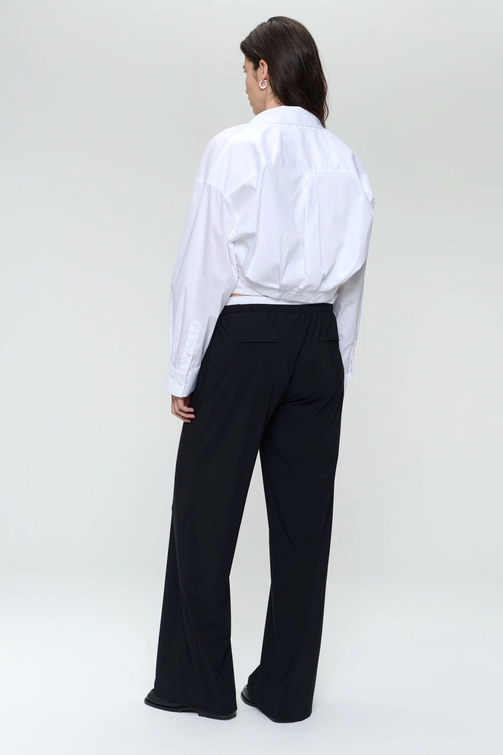Chemise en popeline blanche ample, vue de dos, portée avec un pantalon noir, style moderne et structuré.