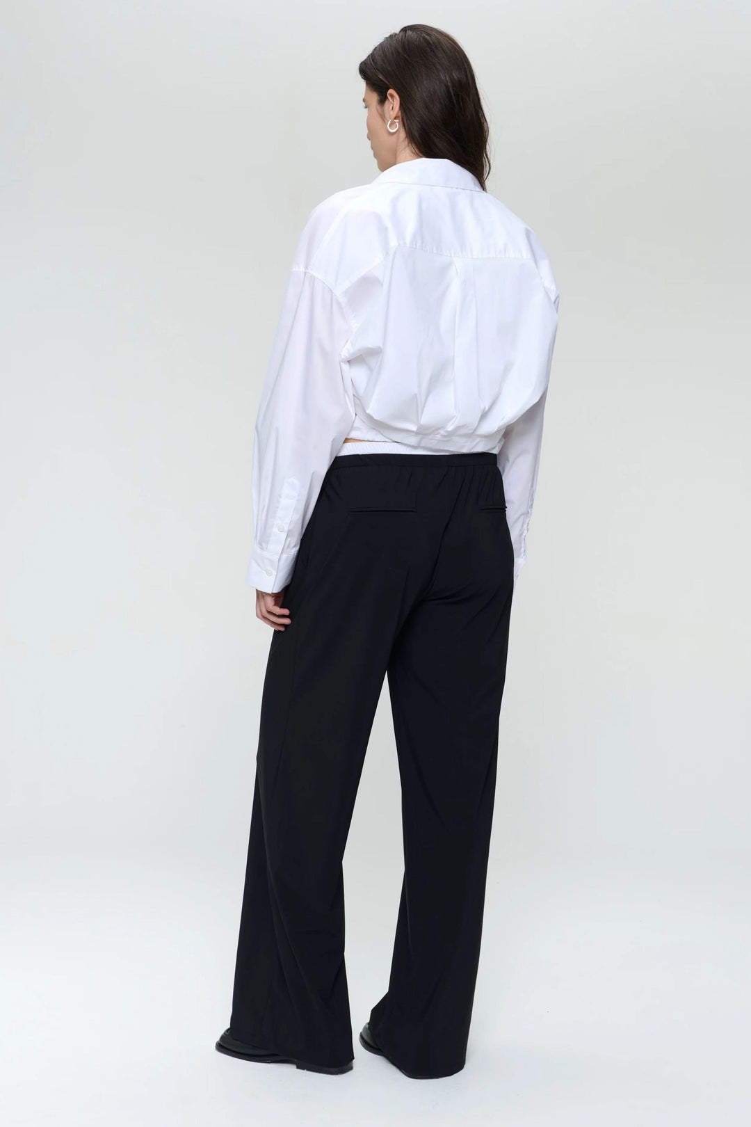 Chemise en popeline blanche ample, vue de dos, portée avec un pantalon noir, style moderne et structuré.