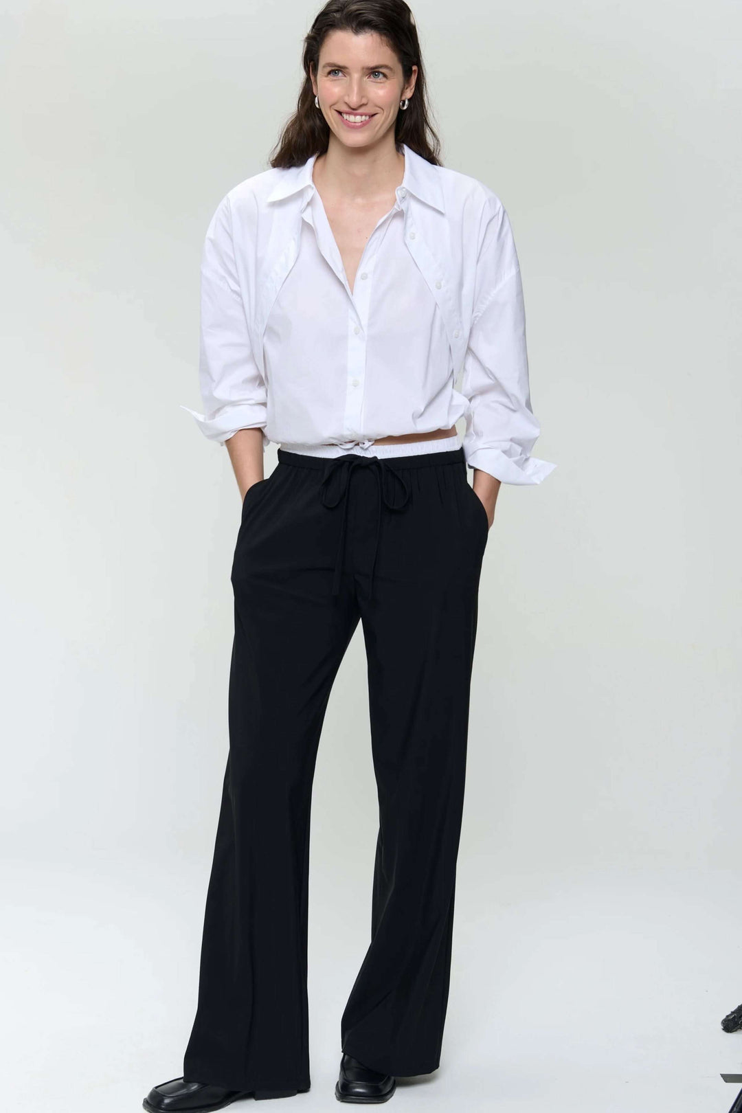 Femme portant une chemise en popeline blanche et un pantalon noir, affichant un look chic et décontracté.