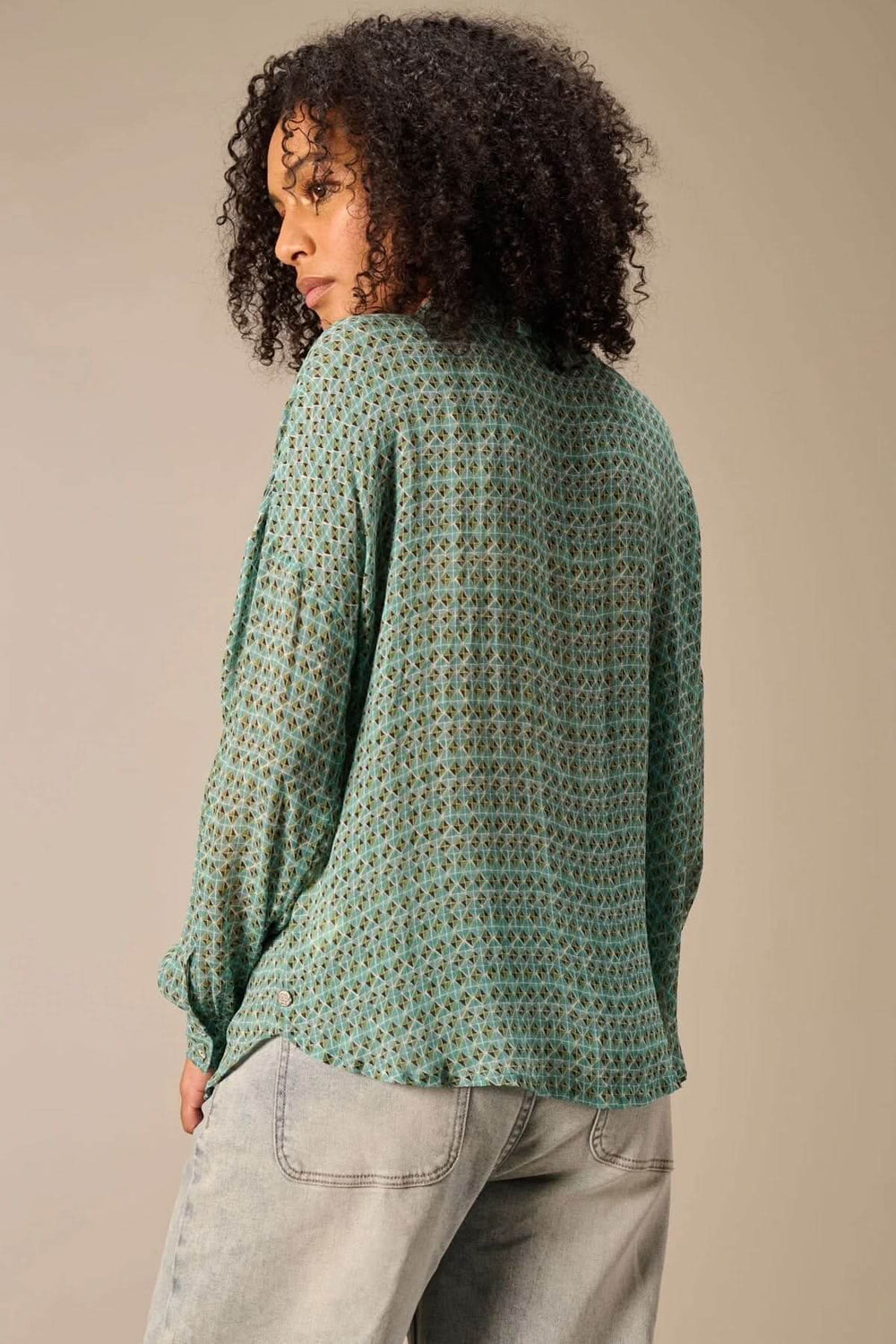 Vue arrière d'une chemise fluide imprimé vert avec un motif géométrique, portée par une femme avec des cheveux bouclés.