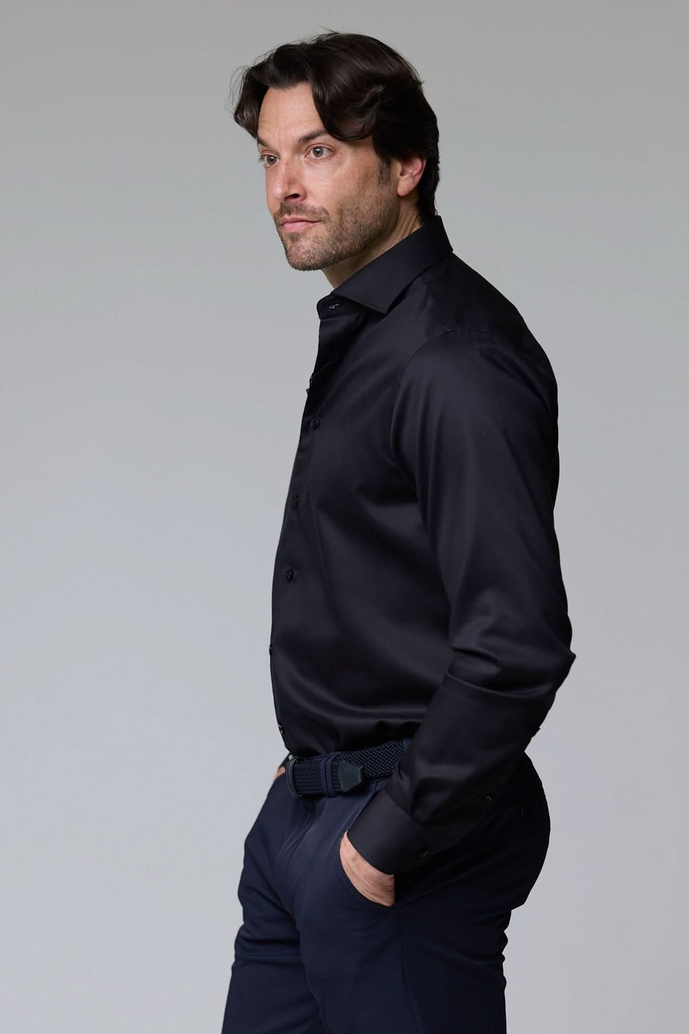 Homme portant une chemise habillée satinée noire avec coupe ajustée et col élégant pour un look sophistiqué et moderne.