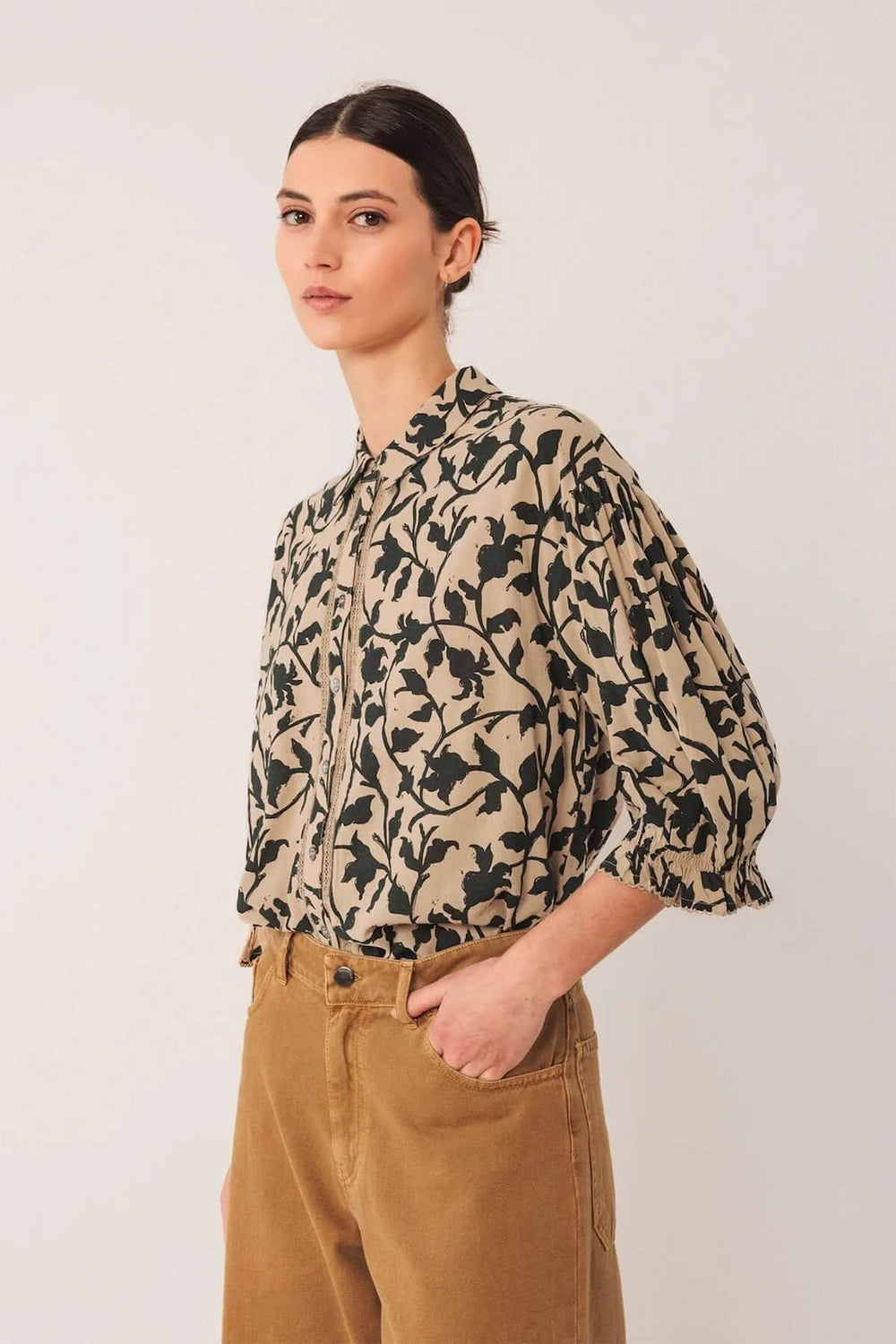 Chemise imprimée à la coupe fluide avec motif végétal, col chemise classique et manches bouffantes, portée avec un pantalon marron.