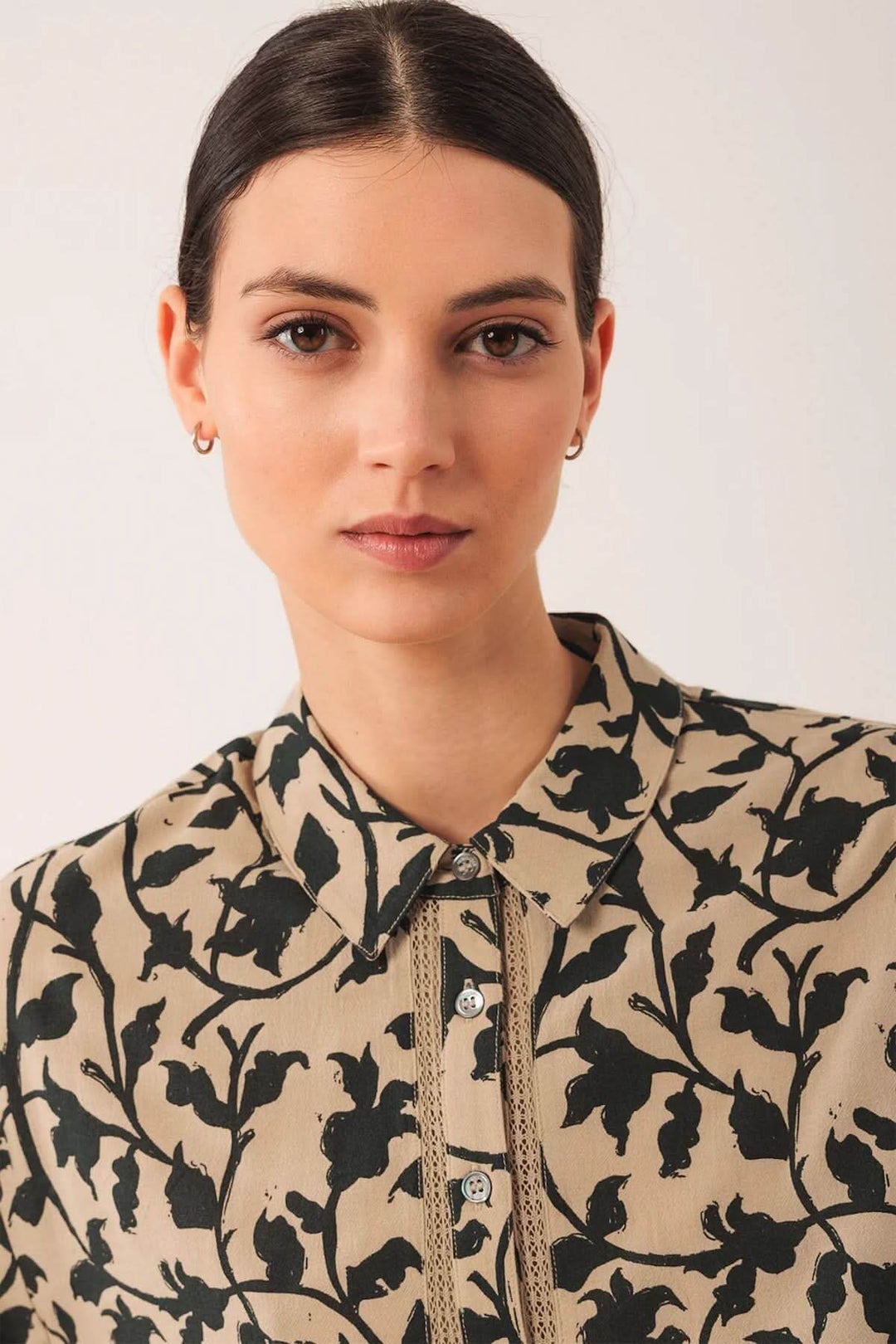 Femme portant une chemise imprimée à motif végétal audacieux, coupe fluide, col chemise classique, manches bouffantes sophistiquées.