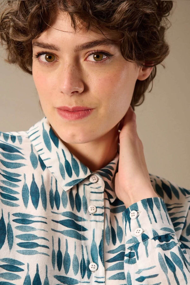 Femme portant une chemise imprimée à manches longues avec un motif graphique bleu et blanc, col classique et boutons visibles.
