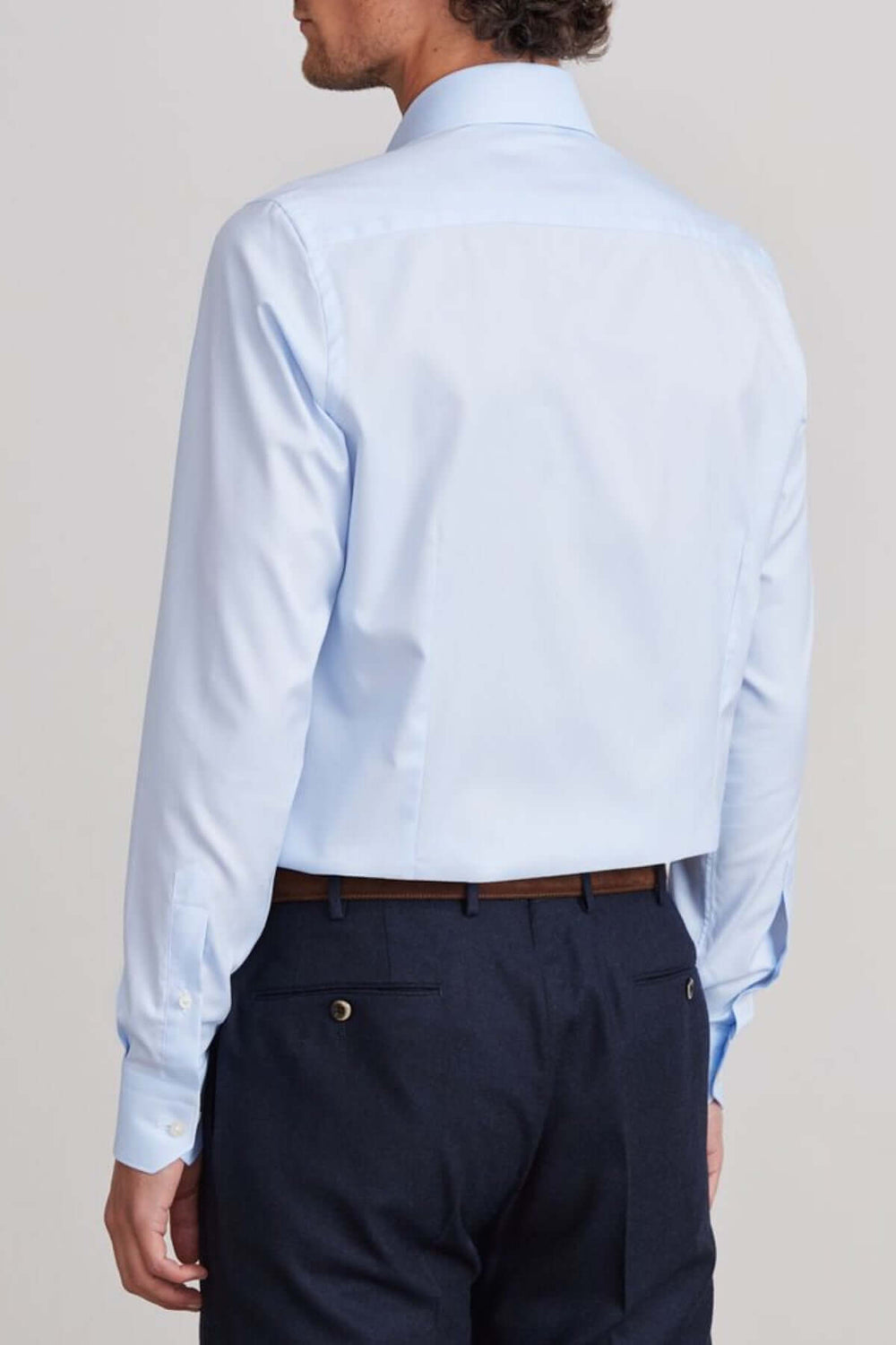 Homme portant une chemise moderne bleu clair, vue de dos, avec pantalon foncé pour un look élégant.
