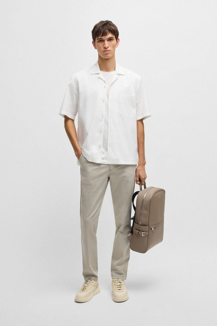 Homme portant une chemise oversize blanche élégante et un sac à dos beige, vêtu d'un look décontracté.
