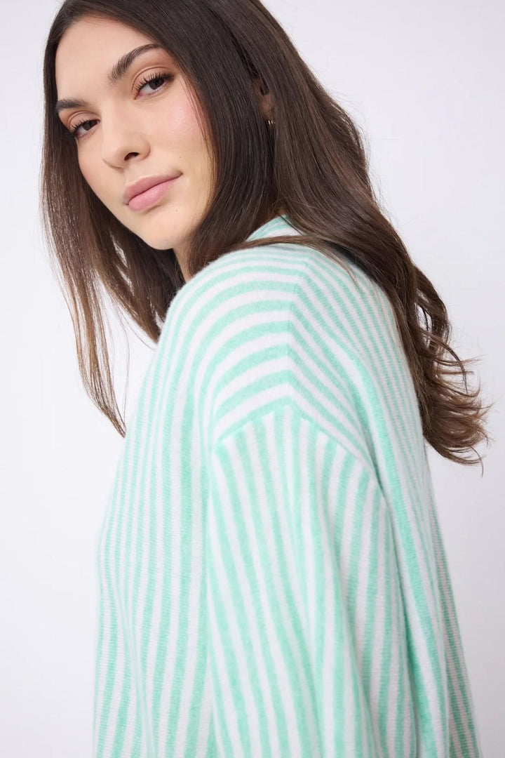 Femme portant une chemise oversize en cachemire à rayures vertes et blanches, vue de côté, style contemporain et élégant.