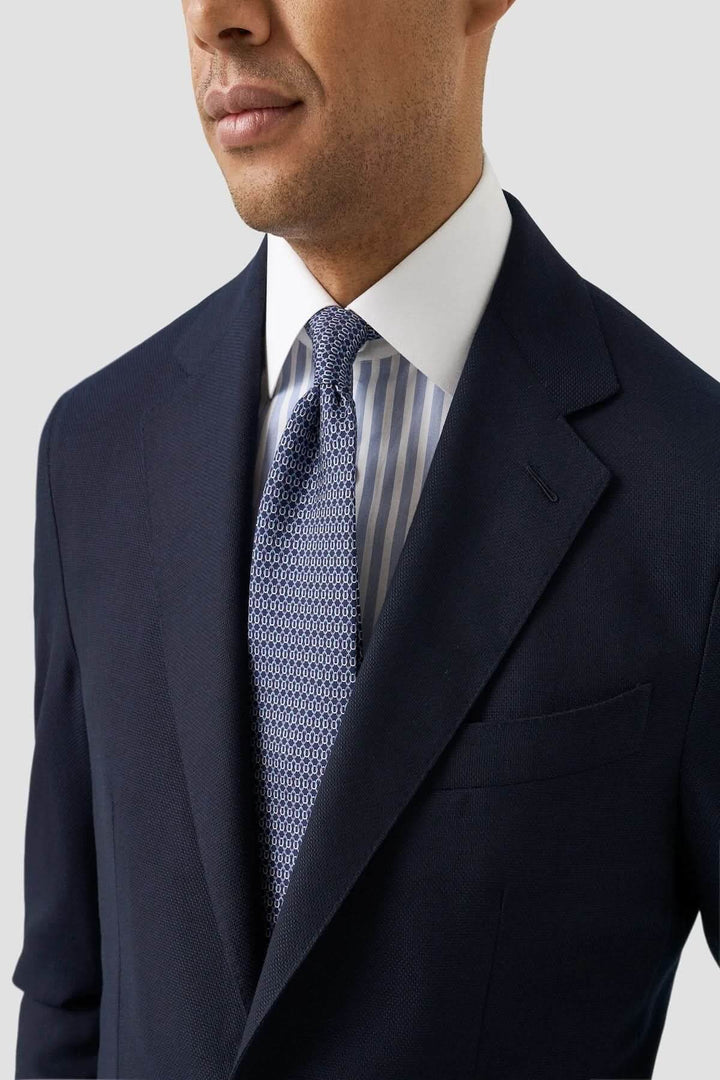 Homme en chemise à rayures Bengal et col blanc, portant un complet foncé et une cravate texturée.